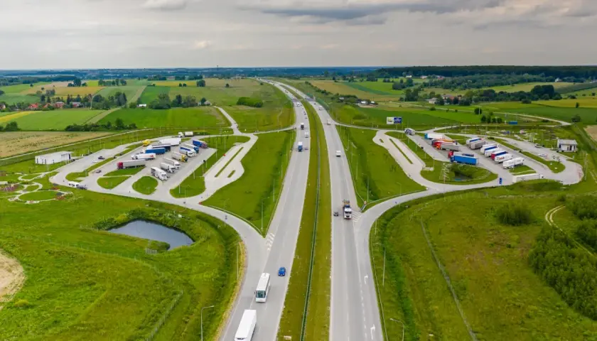 Miejsce obsługi podróżnych (MOP) na autostradzie, z parkingiem dla ciężarówek i samochodów osobowych, otoczone zielenią.