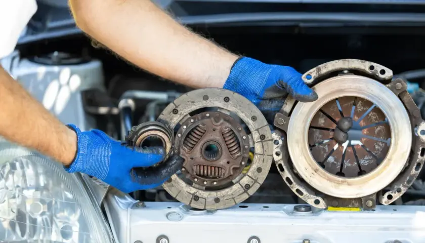 Mechanik w niebieskich rękawiczkach pokazuje zużyte części sprzęgła. Zastanawiasz się, ile kosztuje wymiana sprzęgła?