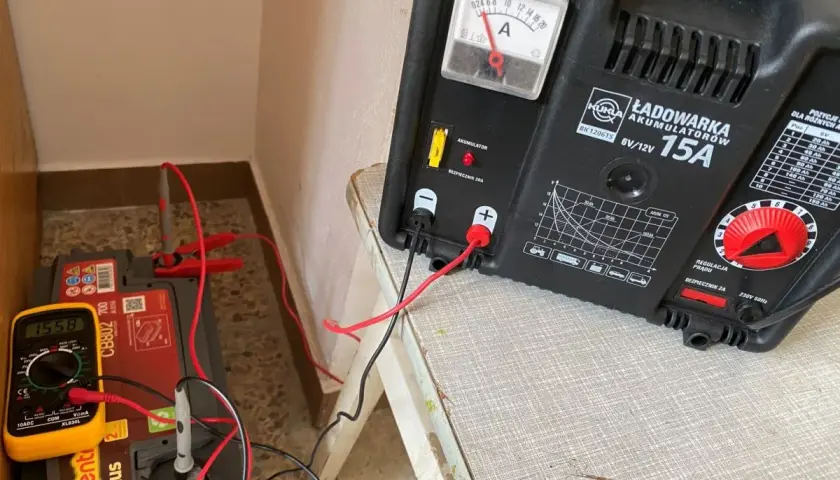 Ładowarka akumulatorów podłączona do akumulatora 6V. Multimetr pokazuje napięcie 15.58V. Instrukcja pokazuje jak ładować akumulator 6v.