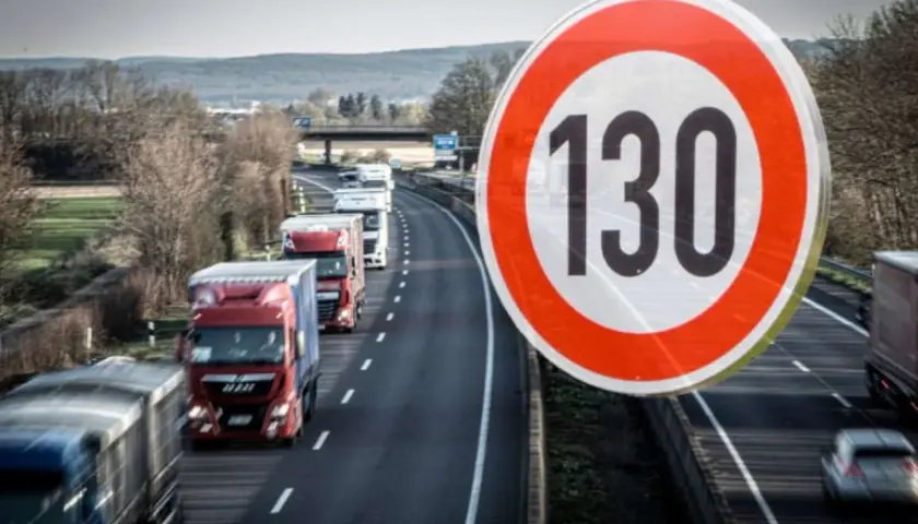 Znak ograniczenia prędkości 130 km/h na niemieckiej autostradzie. Widać sznur ciężarówek jadących w korku.