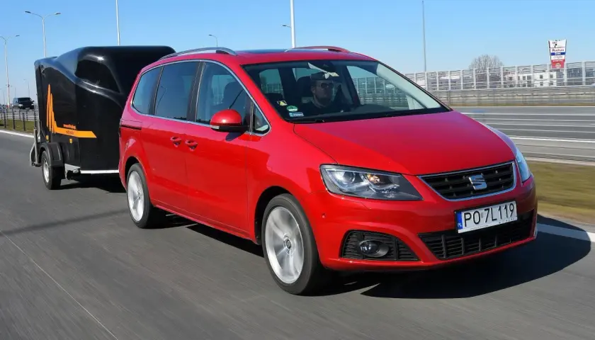Czerwony Seat Alhambra z przyczepą na autostradzie. Zastanawiasz się, ile możesz jechać z przyczepą na autostradzie?