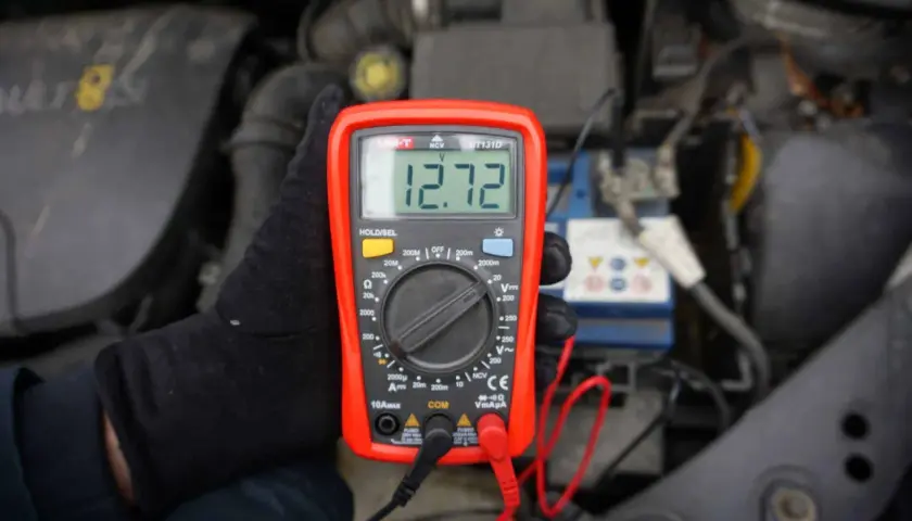 Multimetr pokazuje 12.72V, co jest kluczowe, jak poznać że akumulator jest naładowany. Sprawdzanie napięcia to prosty sposób na ocenę stanu baterii.