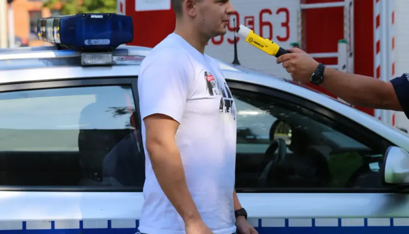 Policjant bada alkomatem mężczyznę stojącego obok radiowozu.