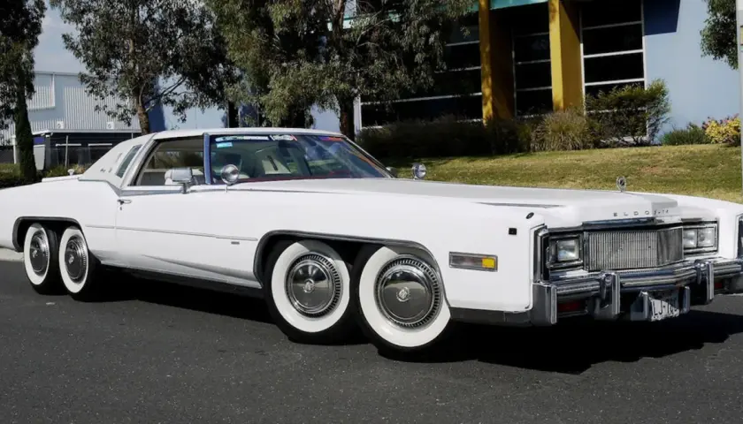 Biały Cadillac Eldorado z podwójnymi kołami z przodu i z tyłu. Ten niezwykły samochód ma aż cztery osie, co czyni go wyjątkowym na drodze.