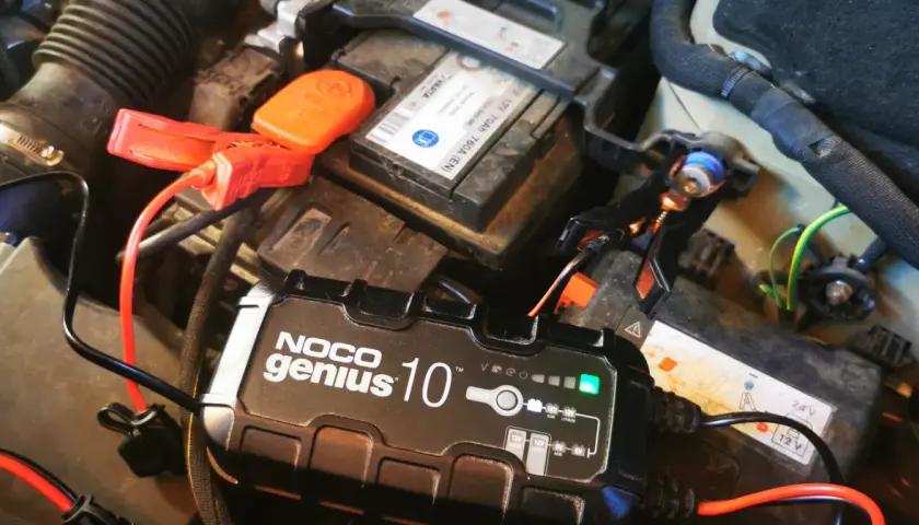 Prostownik NOCO Genius 10 ładuje akumulator samochodowy. Zielona lampka wskazuje, że ładowanie przebiega prawidłowo. Gwiazdka na prostowniku oznacza tryb pracy.