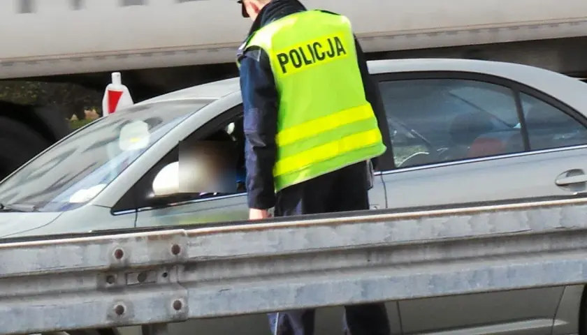 Policjant w kamizelce odblaskowej kontroluje kierowcę. Pamiętaj, że za brak pasów grożą punkty karne.