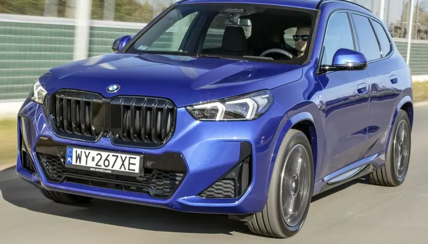 Niebieskie BMW X1 w ruchu drogowym, widok z przodu.