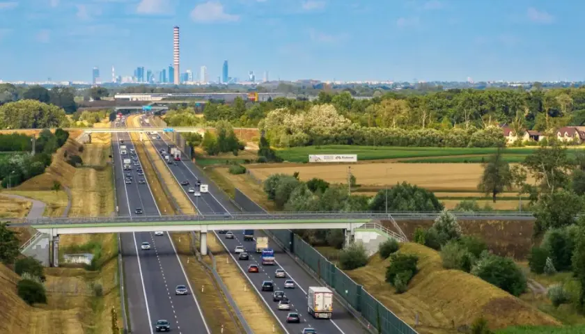 Autostrada z ruchem samochodowym i widocznym w oddali miastem. Pytanie: z jaką prędkością masz obowiązek jechać na autostradzie?