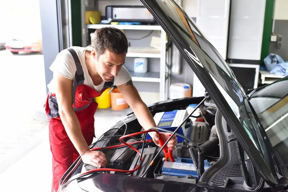 Mechanik podłącza prostownik do akumulatora. Zastanawiasz się, ile kosztuje naładowanie akumulatora u mechanika?