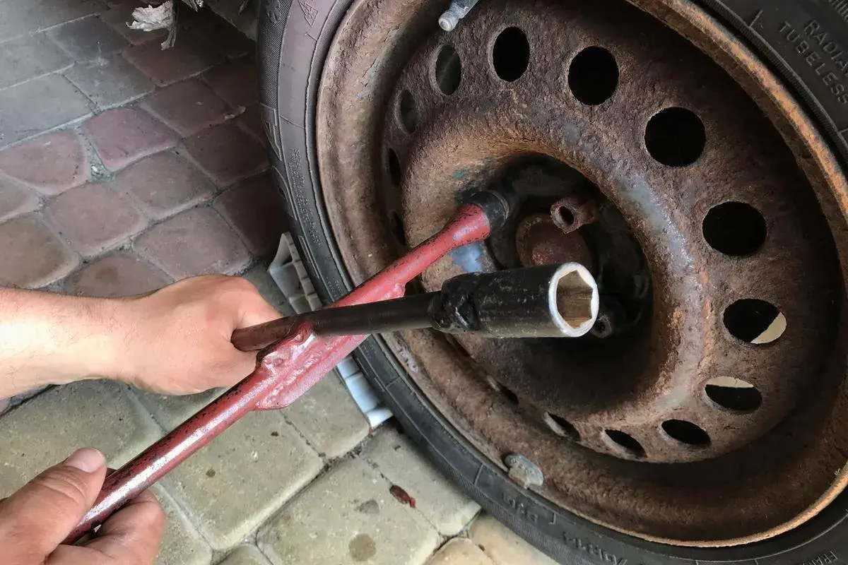 Ręka używa klucza do odkręcenia zapieczonego koła. Rdza na feldze sugeruje, że może to być trudne zadanie.