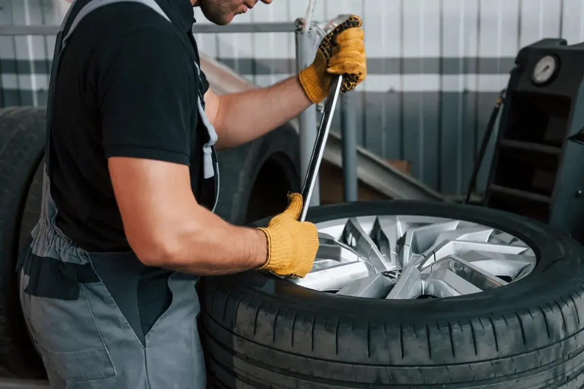 Mechanik w żółtych rękawicach próbuje odkręcić zapieczone koło z piasty za pomocą klucza.