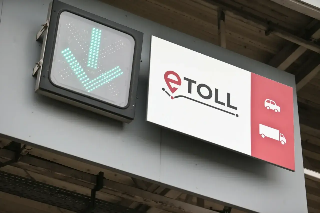 Zielony znak ze strzałkami w dół i logo e-TOLL. Informuje, jak zapłacić za autostradę, wskazując drogę dla samochodów i ciężarówek.