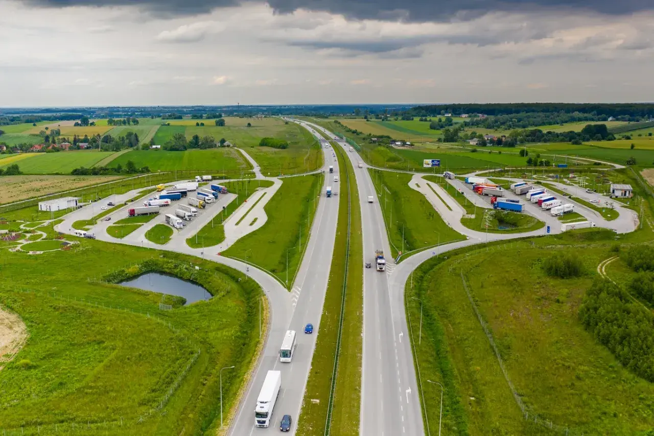 Miejsce obsługi podróżnych (MOP) na autostradzie, z parkingiem dla ciężarówek i samochodów osobowych, otoczone zielenią.