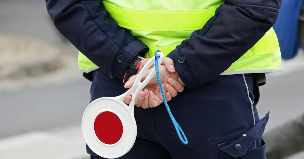 Policjant w kamizelce odblaskowej trzyma znak stop. Zastanawiasz się, ile km można jechać na autostradzie?