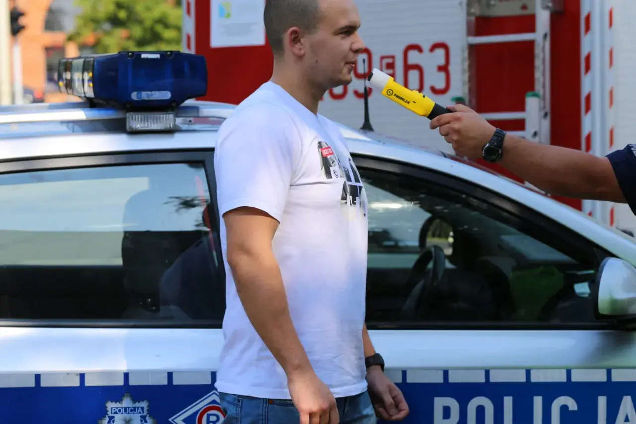 Policjant bada alkomatem mężczyznę stojącego obok radiowozu.
