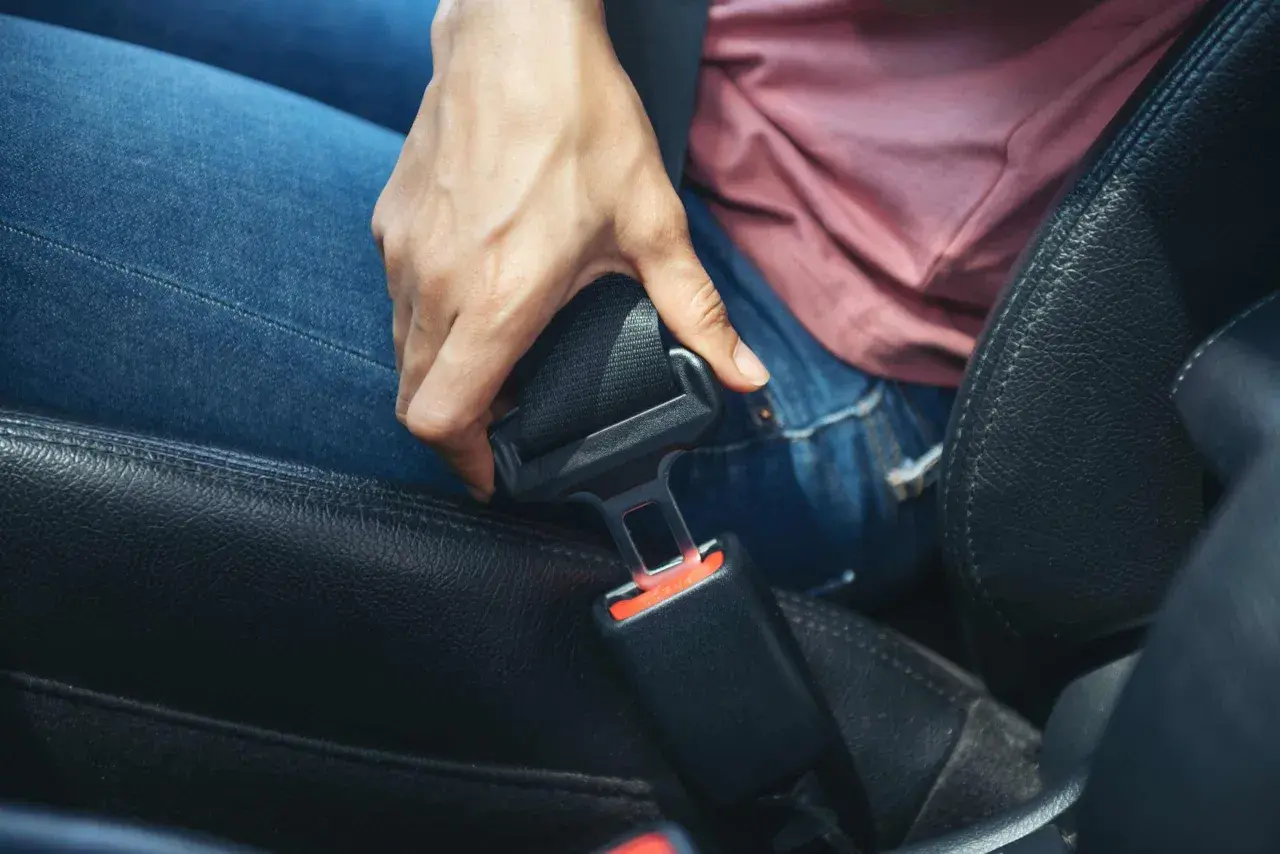 Dłoń próbuje odpiąć pas bezpieczeństwa w samochodzie. Dowiedz się, jak naprawić zablokowany pas bezpieczeństwa, gdy mechanizm nie działa.