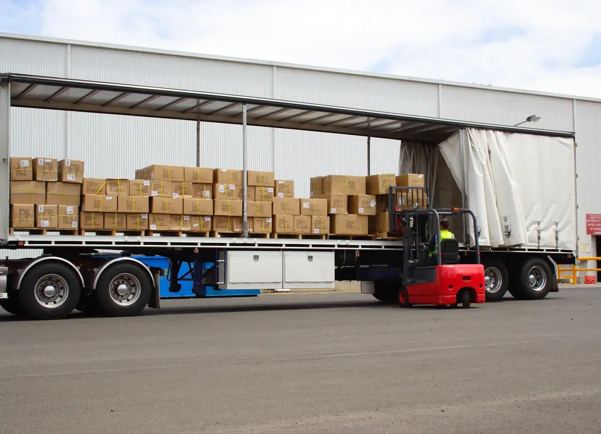 Czerwony wózek widłowy ładuje pudła na naczepę. Taki tir może przewieźć nawet 25 ton ładunku.