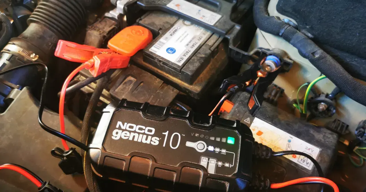Prostownik NOCO Genius 10 ładuje akumulator samochodowy. Zielona lampka wskazuje, że ładowanie przebiega prawidłowo. Gwiazdka na prostowniku oznacza tryb pracy.