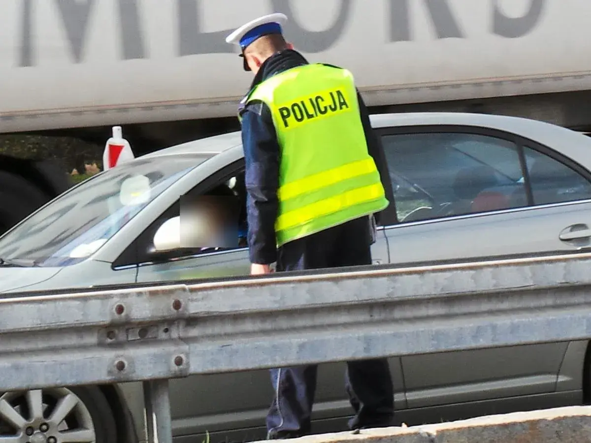 Policjant w kamizelce odblaskowej kontroluje kierowcę. Pamiętaj, że za brak pasów grożą punkty karne.