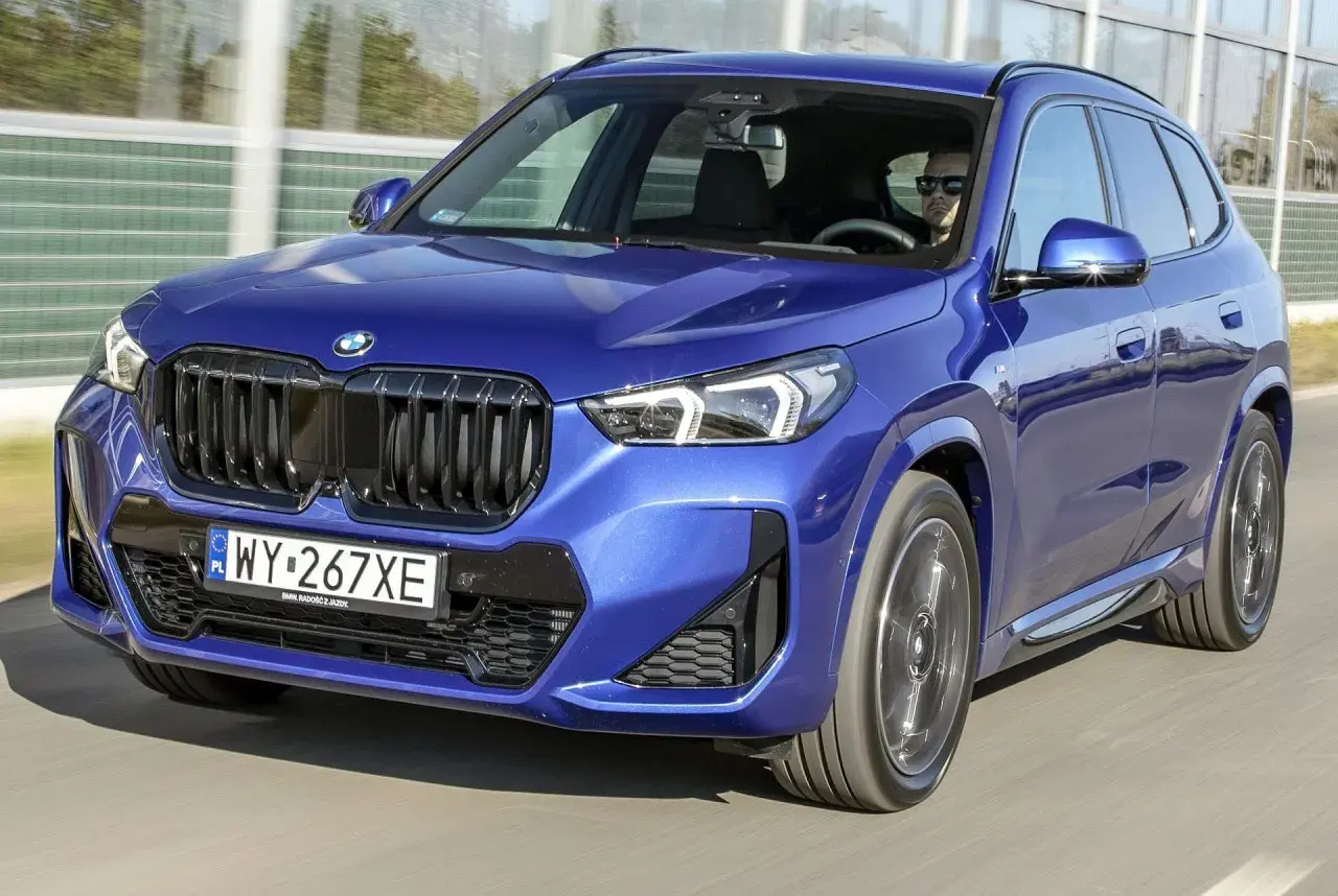 Niebieskie BMW X1 w ruchu drogowym, widok z przodu.