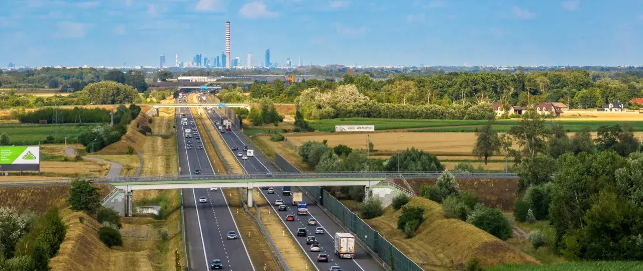 Autostrada z ruchem samochodowym i widocznym w oddali miastem. Pytanie: z jaką prędkością masz obowiązek jechać na autostradzie?
