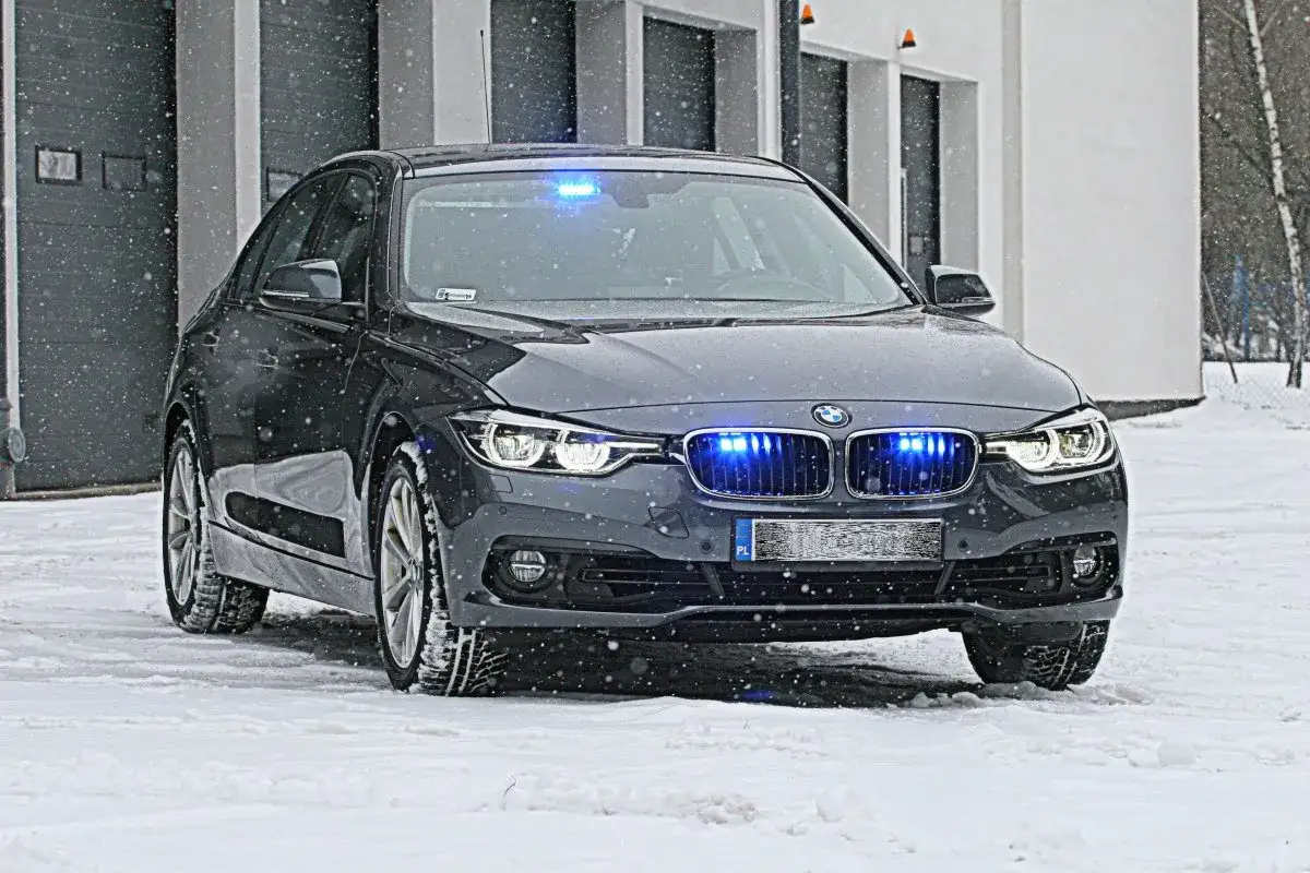 Szary BMW z niebieskimi światłami policyjnymi, gotowy do akcji. To policyjne samochody nieoznakowane, które działają w trudnych warunkach zimowych.
