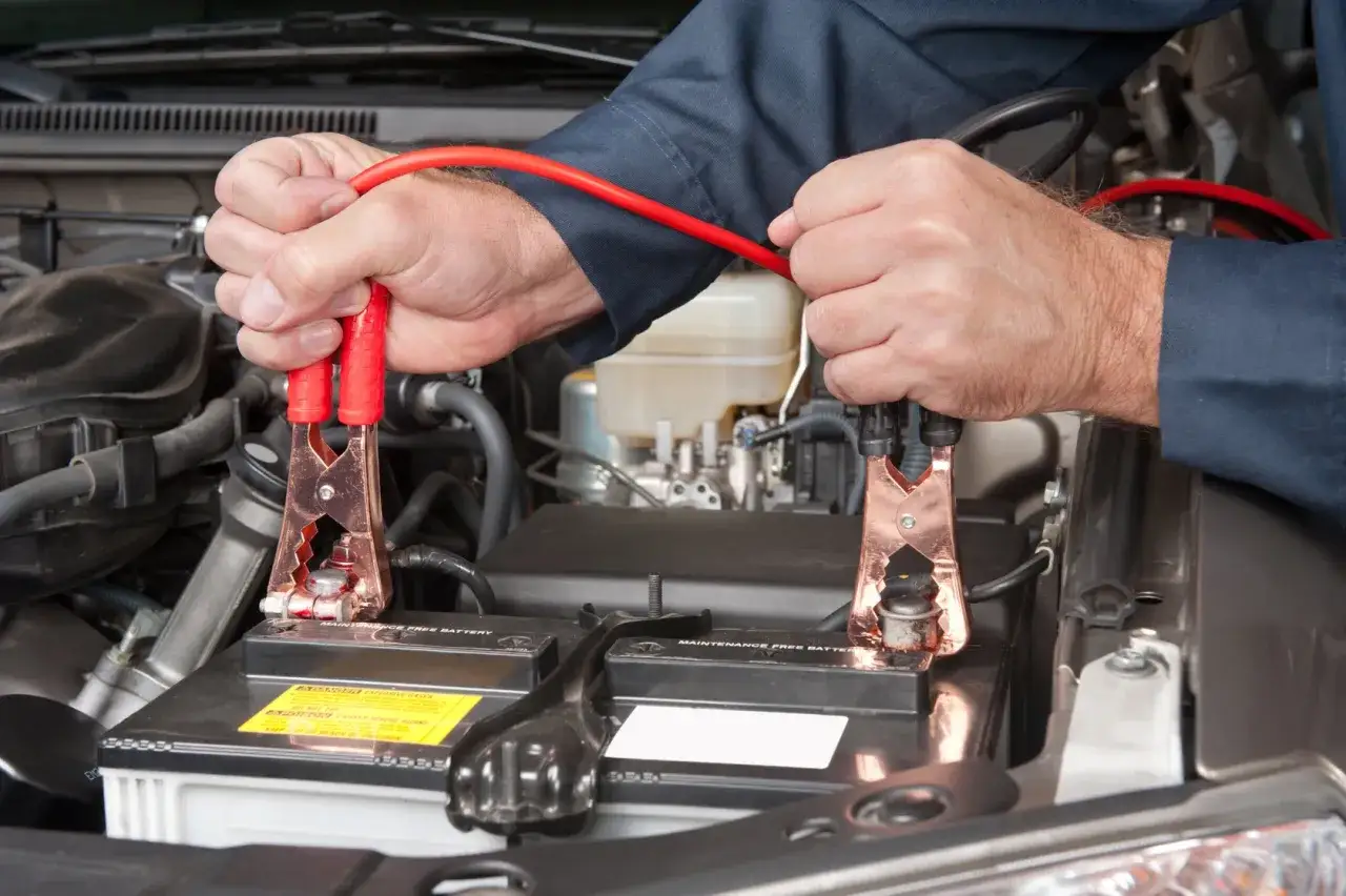 Mechanik podłącza kable rozruchowe do akumulatora bezobsługowego, aby go naładować prostownikiem.