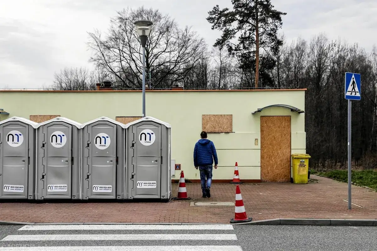 Cztery przenośne toalety stoją obok budynku. Mężczyzna w niebieskiej kurtce idzie w stronę budynku. Co znaczy skrót MOP na autostradzie? To miejsce obsługi podróżnych.