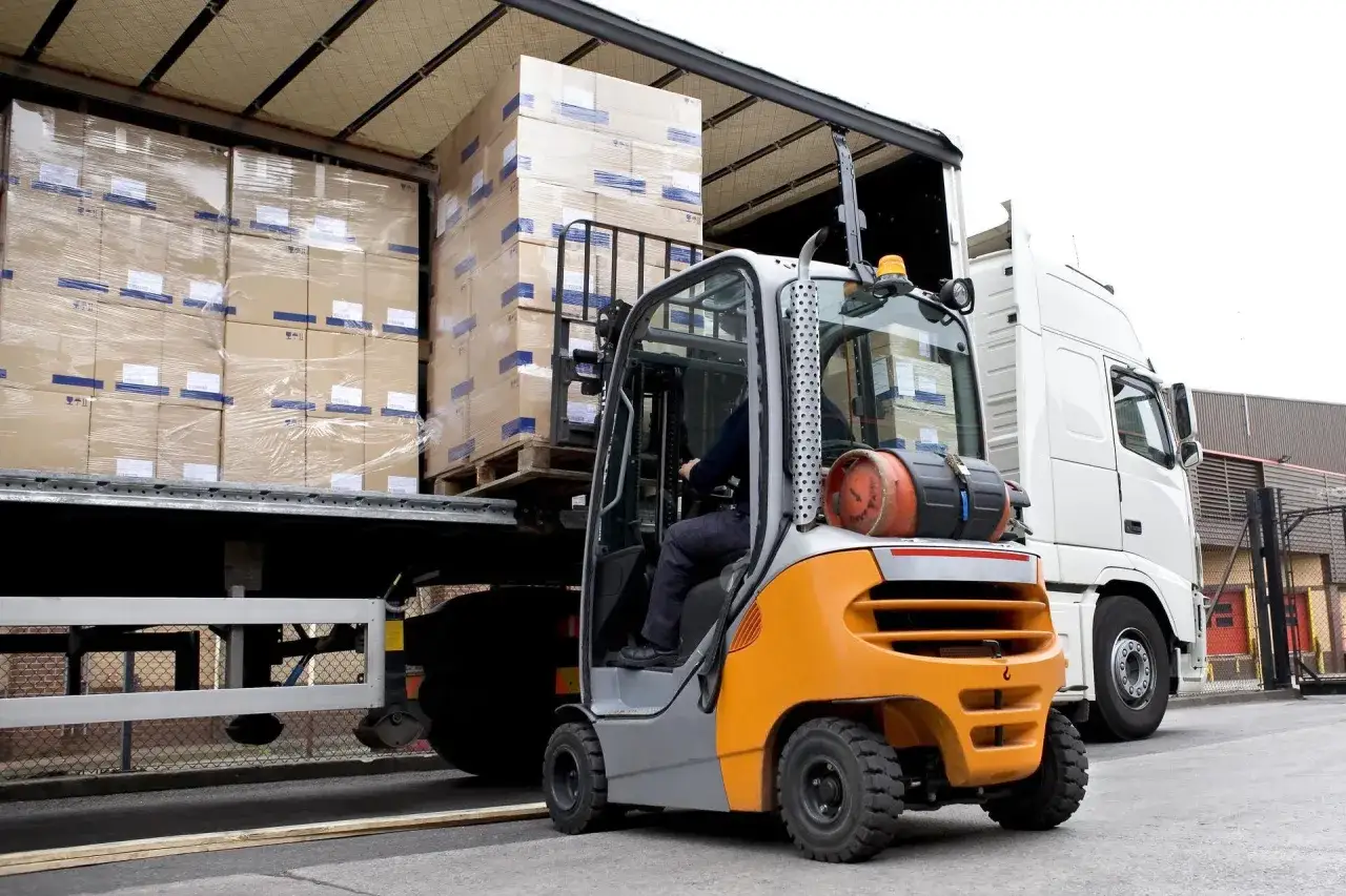 Operator wózka widłowego rozładowuje palety z kartonami. On odpowiada za bezpieczeństwo ładunku podczas transportu.