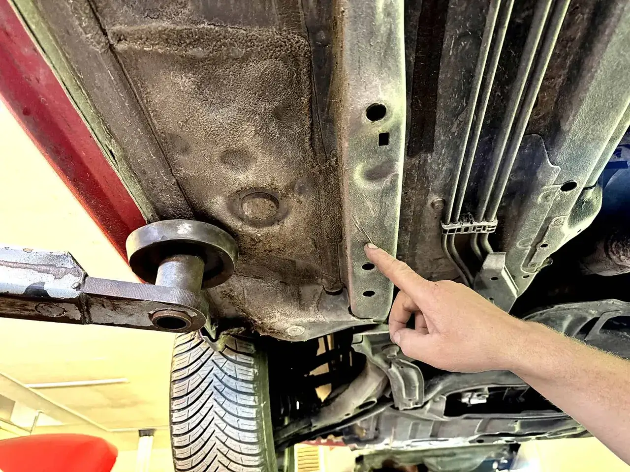 Pokazuję, jak podnieść auto lewarkiem, wskazując wzmocniony próg. To kluczowe miejsce do bezpiecznego podnoszenia pojazdu.